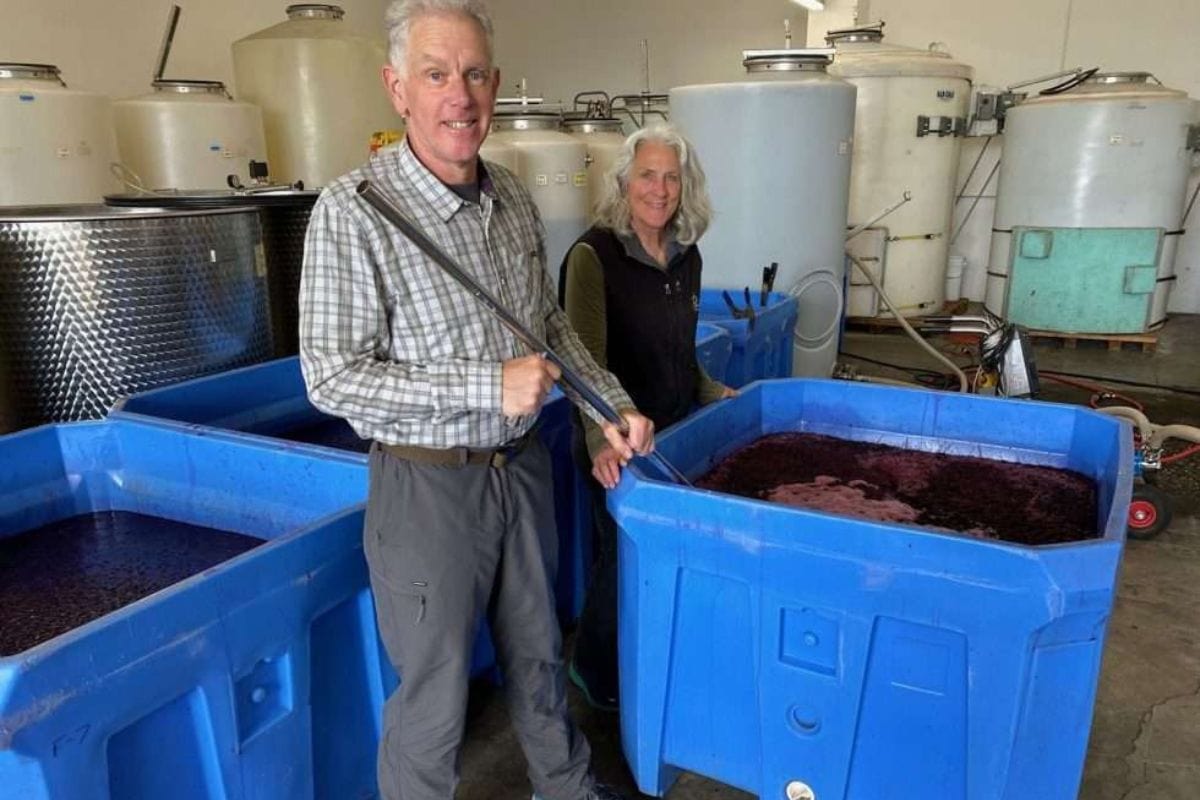 Two adults stirring wine being made at Pasek Winery in a mixing bucket.