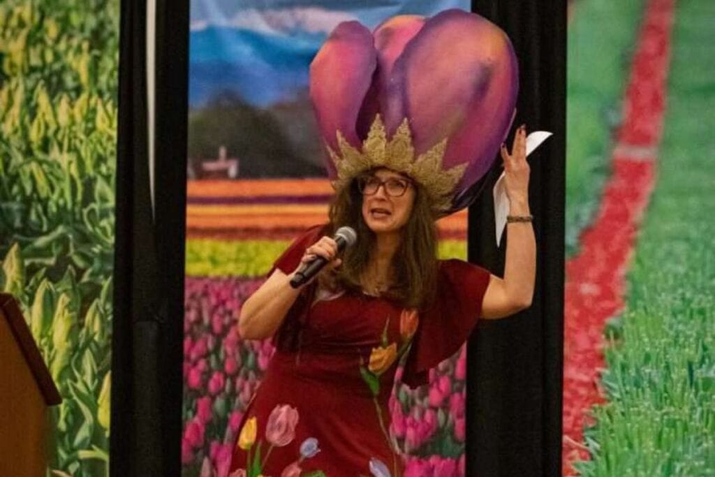 Woman wearing a large tulip crown on stage with a microphone and tulips on her dress.