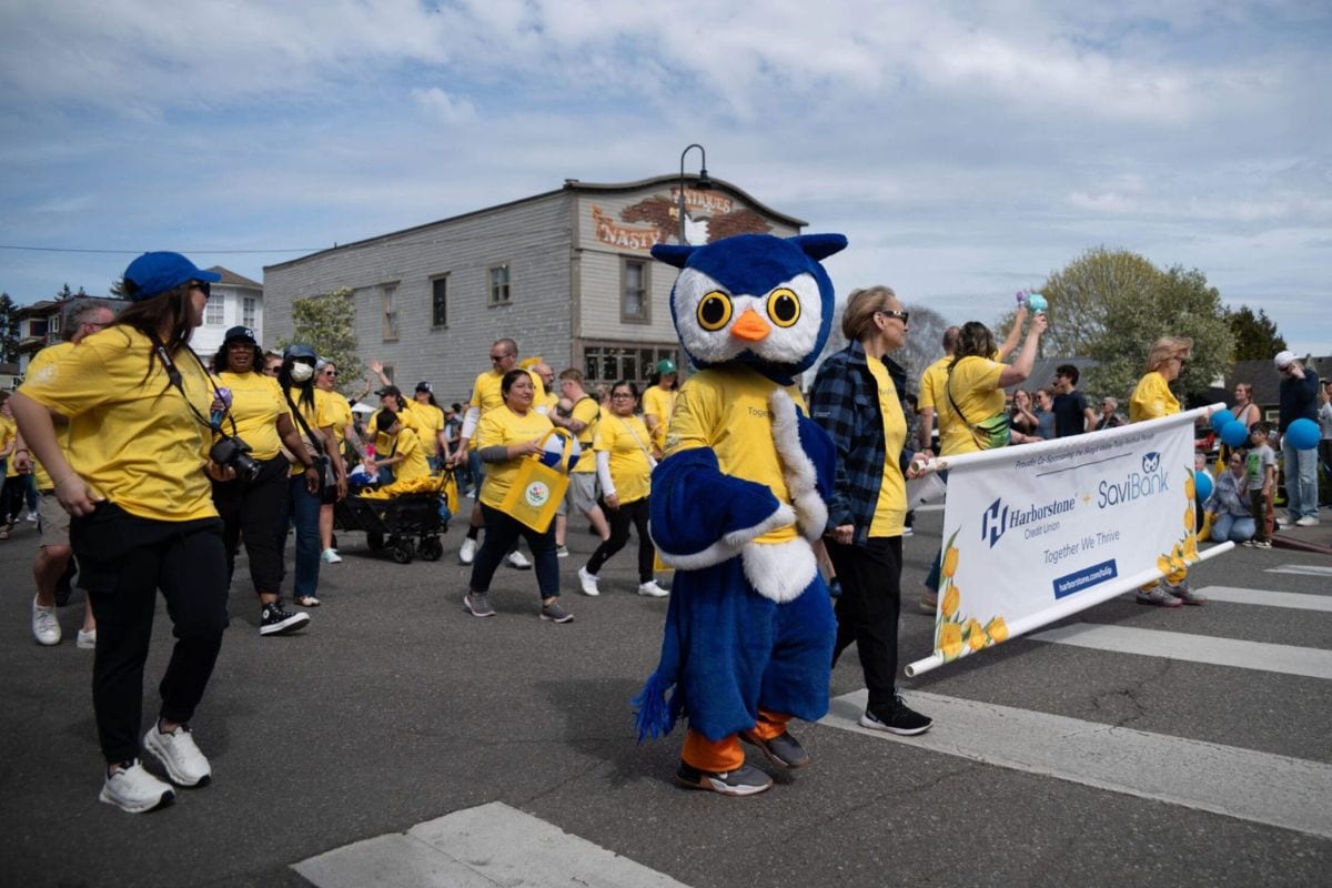 People participating in the Skagit Valley Tulip Festival parade with a mascot and banners.