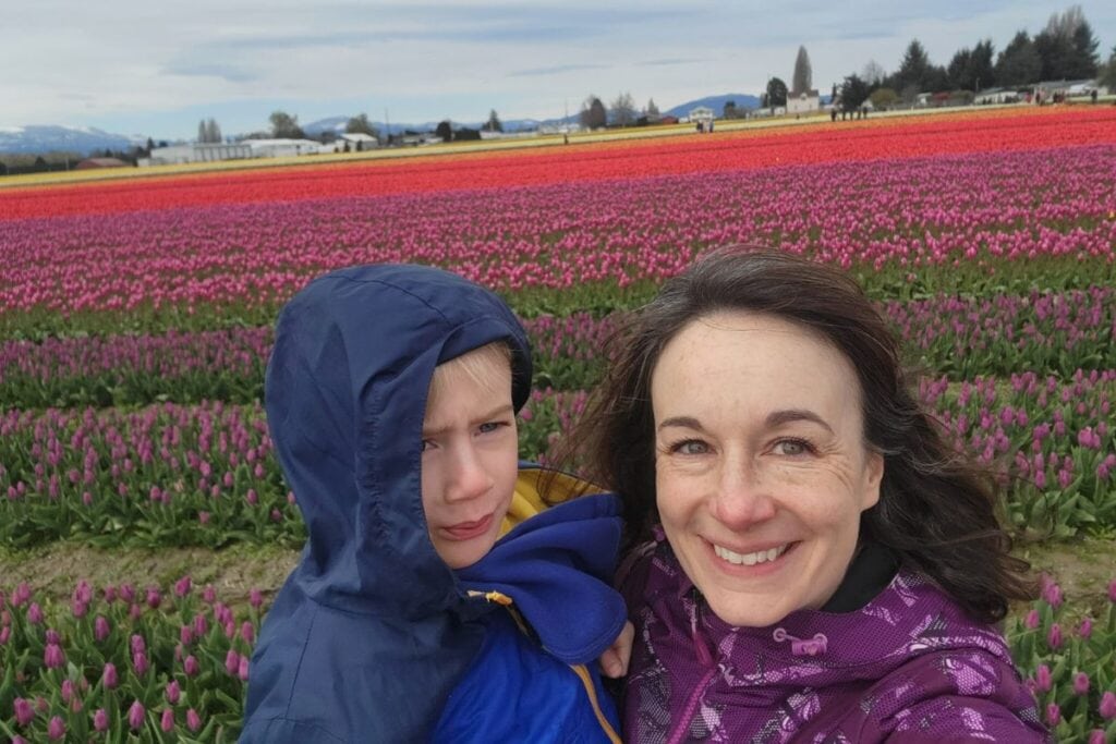 A mother is posing with her son wearing a blue rain jacket posing in front of a field of tulips at the Skagit Valley Tulip Festival.