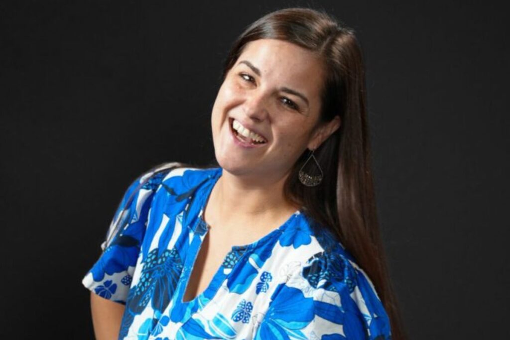 A woman smiles in a blue and white dress in front of a black background
