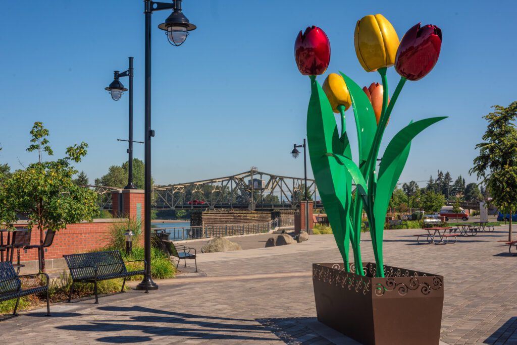 Colorful tulip sculpture on the Mount Vernon Riverwalk overlooking the Skagit River and bridge on a sunny day.